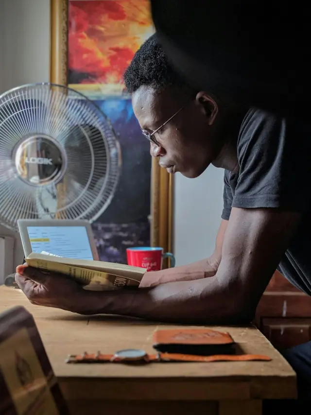 Reader enjoying a paperback book at a wooden desk in soft window light